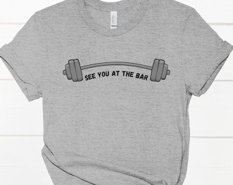 Può includere: Maglietta grigia con una grafica di bilanciere nero e grigio e il testo "See you at the bar".