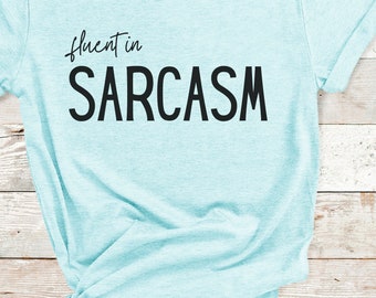 May include: A light blue t-shirt with the text "fluent in SARCASM" printed on the front. The shirt is a heather ice blue color.