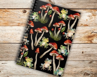 May include: A black spiral notebook with a repeating pattern of red and white mushrooms and green frogs. The background is black.