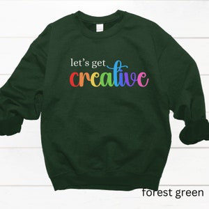 May include: Forest green sweatshirt with the text "let's get creative" in rainbow colors.