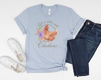 May include: A light blue short-sleeve t-shirt featuring a brown chicken illustration surrounded by a floral wreath and the text "Life is better with Chickens" in a script font, paired with dark blue denim jeans and white canvas sneakers.