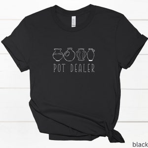 May include: Black t-shirt with a white graphic of five different pottery designs and the text "POT DEALER".