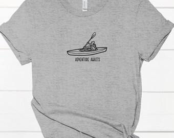 May include: Gray t-shirt with a black line drawing of a person kayaking and the text "Adventure Awaits".