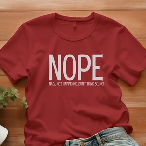 Könnte beinhalten: Rotes T-Shirt mit weißem Text, der "NOPE" und "NADA. NOT HAPPENING. DON'T THINK SO. NO!" lautet.