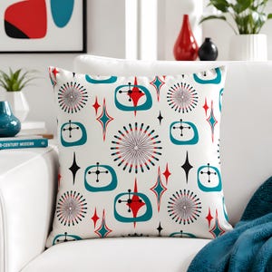 May include: A square throw pillow with a white background featuring a repeating pattern of teal rounded rectangles, red starburst shapes, black starbursts, and thin black lines. The design includes stylized atomic-era motifs in red, teal, and black.