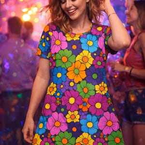 Può includere: Una donna indossa un abito a maniche corte con un vivace motivo floreale. L'abito presenta grandi fiori colorati nelle tonalità di viola, rosa, blu, verde e arancione su uno sfondo viola scuro. La donna sorride in un ambiente festivo.