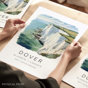 May include: A print depicting the White Cliffs of Dover, with the sea and green fields. The word "DOVER" is printed in black, along with coordinates and "KENT / UNITED KINGDOM". The words "PHYSICAL PRINT" are printed at the bottom.