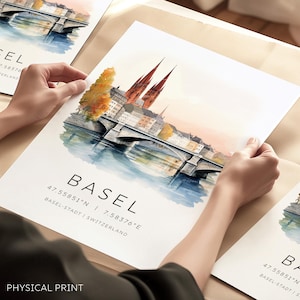 Peut inclure: Une illustration à l'aquarelle de la ville de Bâle, en Suisse. L'illustration représente un pont au-dessus d'une rivière avec des bâtiments et une église en arrière-plan. Le texte "BASEL" est écrit en noir en bas de l'impression, ainsi que les coordonnées "47.55851°N | 7.58376°E" et le texte "BASEL-STADT | SUISSE".