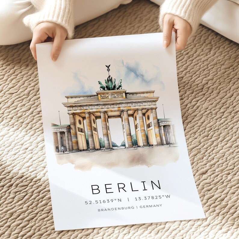 May include: A watercolor illustration of the Brandenburg Gate in Berlin, Germany. The gate is a famous landmark and is depicted in a light yellow color with a blue sky and clouds in the background. The text "BERLIN" is printed below the gate, along with the coordinates "52.51639&deg;N | 13.37825&deg;W" and the words "BRANDENBURG | GERMANY".