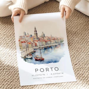 May include: A watercolor painting of the city of Porto, Portugal. The painting shows the city's colorful buildings, the Douro River, and several boats. The text "PORTO" is written in large letters at the bottom of the painting, along with the coordinates "41.15751&deg;N | -8.63706&deg;W" and the text "DISTRITO DE LISBOA | PORTUGAL".