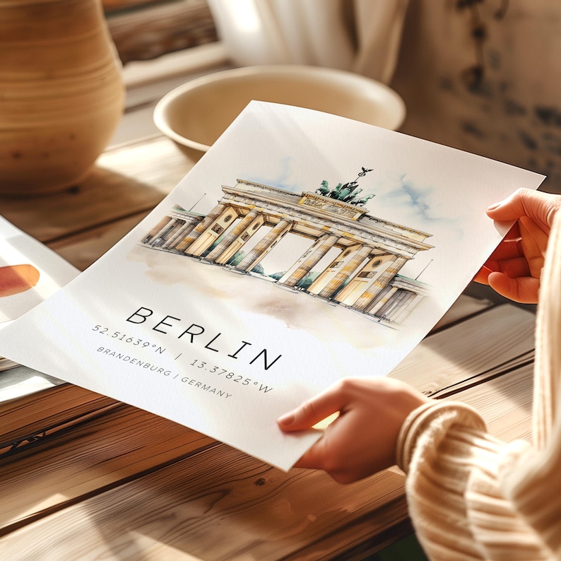 May include: A watercolor illustration of the Brandenburg Gate in Berlin, Germany. The image is on a white background with the text "BERLIN 52.5163&deg;N | 13.37825&deg;W BRANDENBURG | GERMANY" below the illustration.
