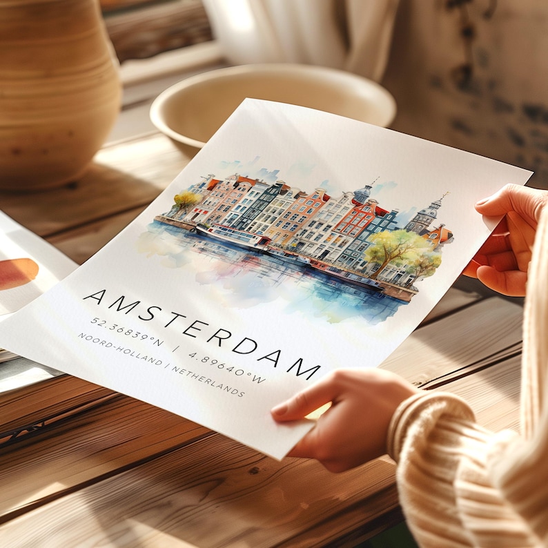 Peut inclure: Une peinture &agrave; l'aquarelle d'Amsterdam, Pays-Bas. La peinture repr&eacute;sente un canal avec des b&acirc;timents color&eacute;s bordant l'eau. Le texte "AMSTERDAM 52.3685&deg;N | 4.8964&deg;W NOORD-HOLLAND | NETHERLANDS" est imprim&eacute; sous l'image.