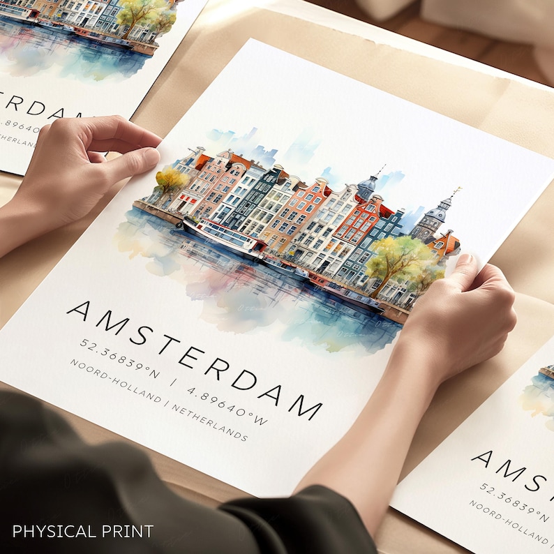 Peut inclure: Une peinture &agrave; l'aquarelle de l'horizon d'Amsterdam avec des b&acirc;timents color&eacute;s le long d'un canal. Le texte "AMSTERDAM" est &eacute;crit en noir au bas de l'impression, ainsi que les coordonn&eacute;es "52.36839&deg;N | 4.89640&deg;W" et l'emplacement "NOORD-HOLLAND | PAYS-BAS". Le texte "PHYSICAL PRINT" est &eacute;crit en noir au bas de l'impression.