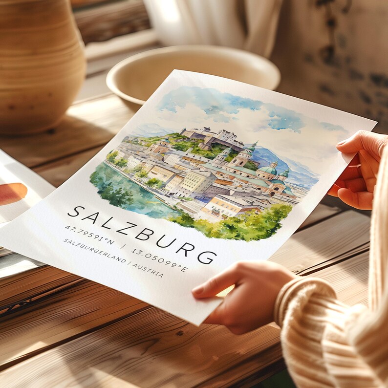 Peut inclure: Une peinture &agrave; l'aquarelle de Salzbourg, en Autriche. La peinture repr&eacute;sente l'horizon de la ville, y compris la forteresse de Hohensalzburg, la rivi&egrave;re Salzach et les montagnes environnantes. La peinture est encadr&eacute;e dans un passe-partout blanc et porte le texte "SALZBURG 47.79591&deg;N | 13.05099&deg;E SALZBURGERLAND | AUSTRIA" imprim&eacute; sous l'image.