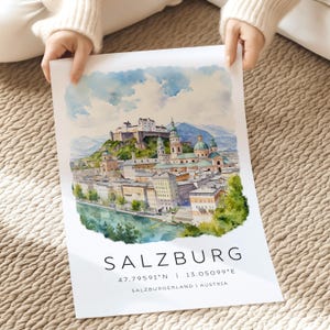 Peut inclure: Une peinture &agrave; l'aquarelle de Salzbourg, en Autriche. La peinture repr&eacute;sente la forteresse embl&eacute;matique de la ville, Hohensalzburg, perch&eacute;e au sommet d'une colline surplombant la ville. La peinture pr&eacute;sente &eacute;galement la rivi&egrave;re Salzach, qui traverse la ville. Le texte "SALZBURG 47.79591&deg;N | 13.05099&deg;E SALZBURGERLAND | AUSTRIA" est imprim&eacute; sous la peinture.