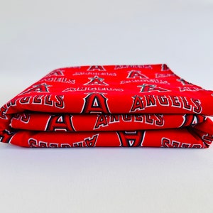 Puede incluir: Tela roja doblada con un patr&oacute;n repetido blanco y negro del logotipo del equipo de b&eacute;isbol de los &Aacute;ngeles Angels.