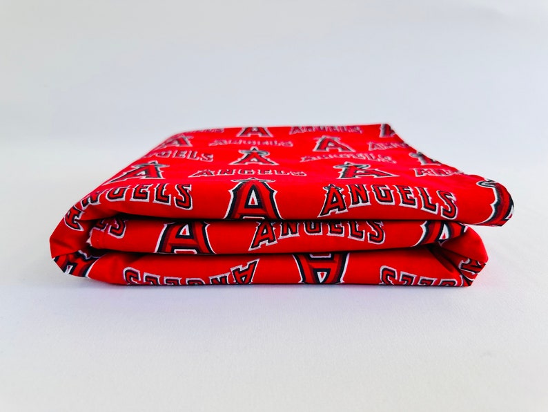 Puede incluir: Tela roja doblada con un patr&oacute;n repetido blanco y negro del logotipo del equipo de b&eacute;isbol de los &Aacute;ngeles Angels.