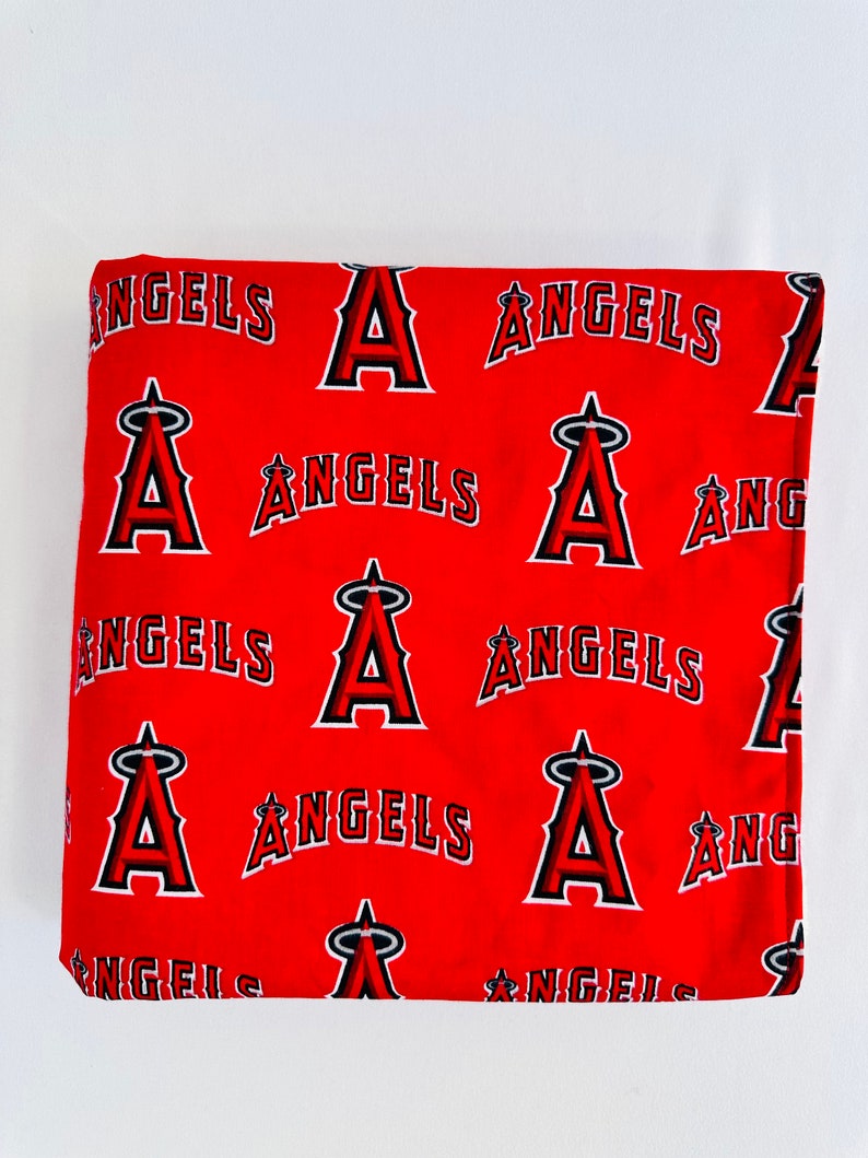 Puede incluir: Tela roja con un patr&oacute;n repetido del logotipo del equipo de b&eacute;isbol de los &Aacute;ngeles &Aacute;ngeles. El logotipo es una 'A' estilizada con alas y la palabra '&Aacute;ngeles' debajo.