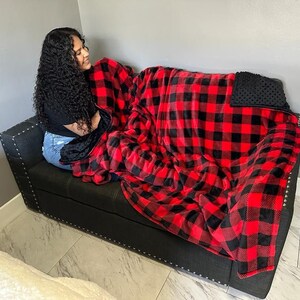 May include: A red and black plaid fleece blanket with a black weighted side. The blanket is on a black couch.