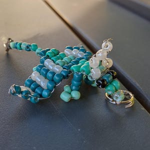 May include: A beaded dragon figurine made with blue, green, and white beads. The dragon is made of wire and has a curled tail.