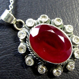 May include: A silver pendant necklace with a large oval-shaped red gemstone surrounded by smaller clear gemstones.