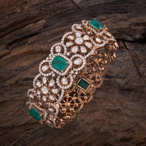May include: A gold bangle bracelet with a delicate design featuring emerald green gemstones and sparkling diamonds.