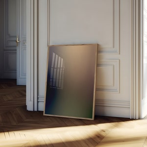 May include: A framed abstract print with a gradient of colors from blue to green to brown. The print is leaning against a white wall in a room with hardwood floors.