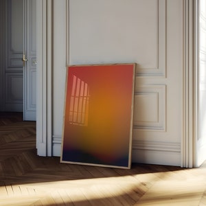 May include: A framed abstract print with a gradient of orange, red, and yellow colors. The print is leaning against a white wall in a room with hardwood floors.