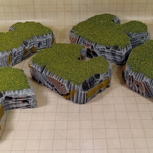 Puede incluir: Cinco islas rocosas en miniatura con musgo verde en la parte superior. Las islas están hechas de material texturizado gris y marrón. Son perfectas para juegos de mesa.