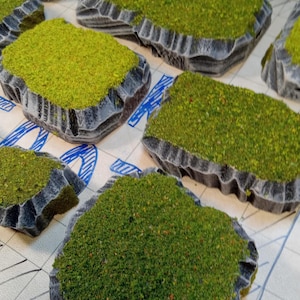 May include: A set of eight miniature, rocky, green, grassy terrain pieces for tabletop gaming or model building.