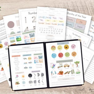 May include: A collection of educational worksheets and a black binder featuring printed charts for days of the week, months, numbers, shapes, and weather. The pages include watercolor illustrations of emotions, seasonal activities, and moon phases with text.