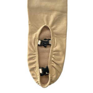 May include: A close-up of the bottom of a beige fabric chair cover with two black plastic clips. The cover has a gathered elastic edge.