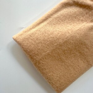 May include: A close-up of a light brown fuzzy fabric. The fabric has a soft, plush texture.