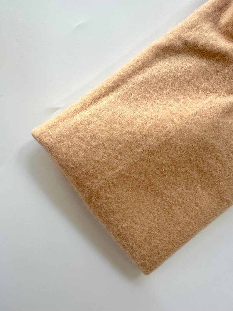 May include: A close-up of a light brown fuzzy fabric. The fabric has a soft, plush texture.