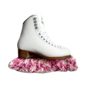 May include: White figure skate boot with a brown sole resting on a pink and white fluffy skate guard.