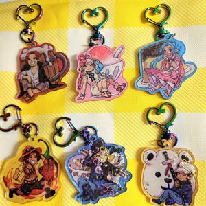 Może przedstawiać: Sześć kolorowych breloków z postaciami z anime. Każdy brelok przedstawia inną postać i tło. Breloki są wykonane z przezroczystego plastiku z holograficznym wykończeniem.