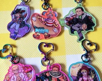 May include: Six colorful holographic keychains featuring anime characters. Each keychain has a different character and design, including a pirate, a clown, a chef, and a donut. The keychains are attached to silver heart-shaped clasps.