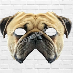 Puede incluir: Una máscara de cara de perro pug marrón y negro con recortes para los ojos. La máscara está hecha de papel y está diseñada para ser usada sobre la cara.