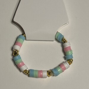 May include: A colorful beaded bracelet with pastel pink, blue, and green beads and gold accents. The bracelet is displayed on a white card with a hole for hanging.