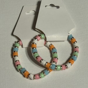 May include: Two colorful beaded bracelets with pastel pink, green, blue, and orange beads. The bracelets are on a white card with a hole for hanging.