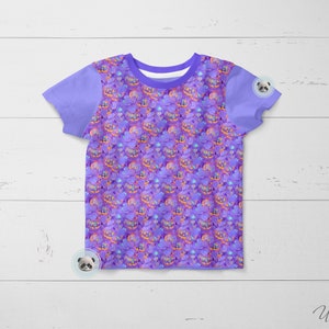 May include: A purple short-sleeved t-shirt with a repeating pattern of purple, orange, and yellow jack-o'-lanterns. The shirt has a plain purple collar and sleeves.