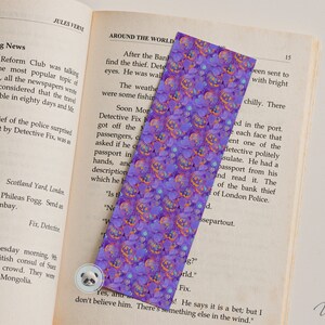 May include: A purple and orange bookmark with a repeating pattern of jack-o'-lantern faces. The bookmark is made of a soft, textured material and has a slightly glittery finish.