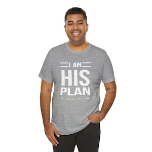Puede incluir: Una camiseta gris jaspeada con el texto "I AM HIS PLAN" en letras blancas. El texto "The Nomad Collective" tambi&eacute;n est&aacute; impreso en letras blancas debajo del texto principal.