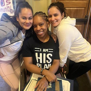Puede incluir: Tres mujeres sonriendo juntas. La mujer del medio est&aacute; sentada en una silla de ruedas y lleva una camiseta negra que dice "I AM HIS PLAN". Las mujeres sostienen certificados y premios.