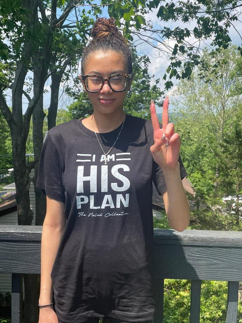 Puede incluir: Una camiseta negra con texto blanco que dice "I AM HIS PLAN The Nelah Collection".