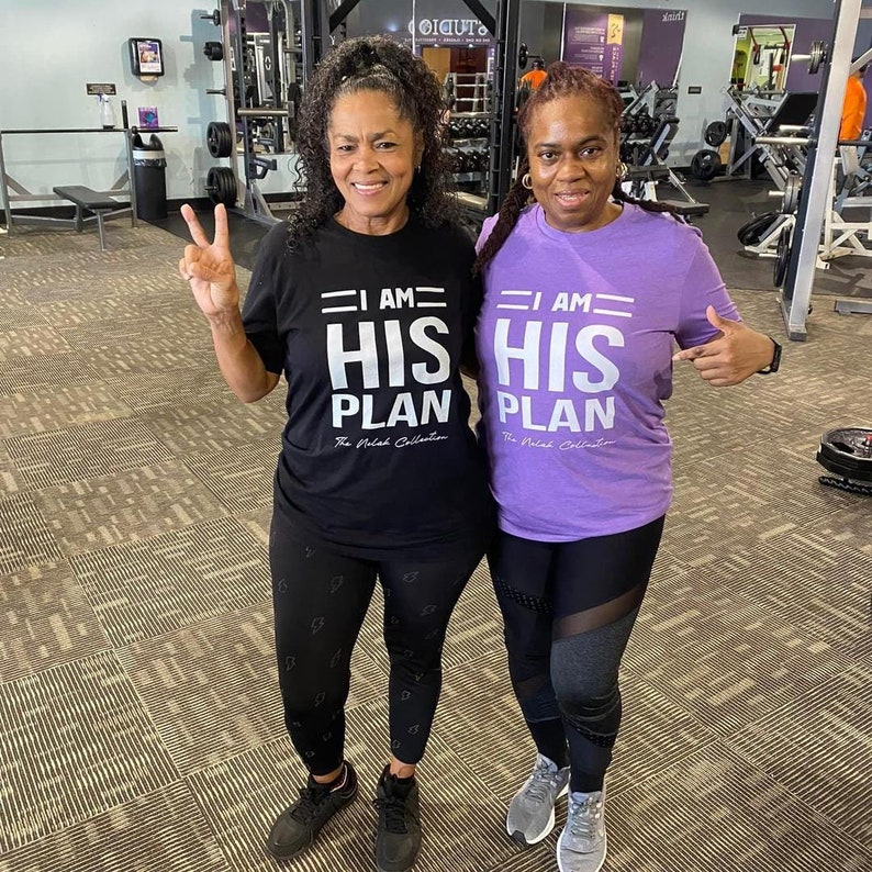 Puede incluir: Dos personas con camisetas negras y moradas con el texto "I AM HIS PLAN" en blanco. La persona de la izquierda lleva leggings negros con un patr&oacute;n y la persona de la derecha lleva leggings negros con paneles de malla. Ambas personas sonr&iacute;en y miran a la c&aacute;mara.