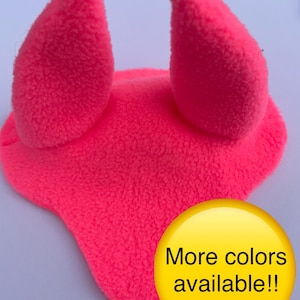 May include: Bright pink horse bonnet with ear covers. The bonnet is made of a soft, textured material. A yellow circle with the text "More colors available!!" is in the lower right corner.