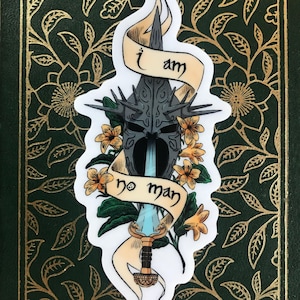 May include: A sticker featuring a stylized illustration of a helmet, sword, and flowers. The text "I am no man" is written on a banner. The design includes a dark helmet, a blue sword, and orange flowers.
