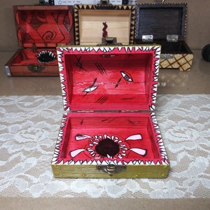 Può includere: Un piccolo forziere di legno con un design dipinto in rosso e bianco. Il forziere è aperto e l'interno è dipinto di rosso con un design di bocca di mostro in bianco e nero.