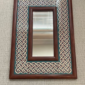 Puede incluir: Un espejo rectangular con un marco de madera y un borde decorativo de azulejos azules, rojos y blancos. Los azulejos presentan un diseño de nudo celta.